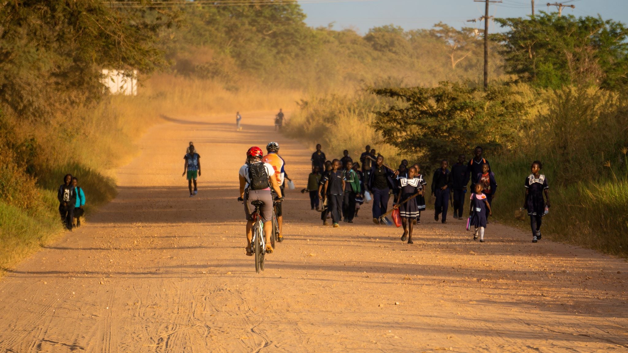 Samuel Roy on a bicycle on a dirt road with many African students